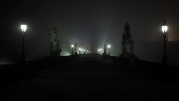 licht in de lantaarn van straatverlichting op de Karelsbrug en mist 's nachts en silhouetten van voetgangers en lopers op de kasseistrook op de brug in de opkomende mist' s nachts. - Video
