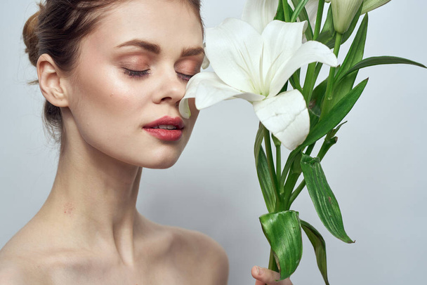 mooi meisje met een boeket van witte bloemen op een lichte achtergrond naakt schouders schoon huid lente - Foto, afbeelding