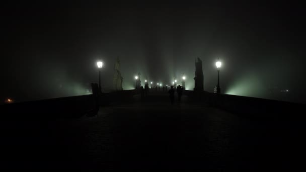 luz na lanterna de iluminação pública na Ponte Charles e nevoeiro à noite e silhuetas de pedestres e corredores no pavimento de paralelepípedos na ponte no nevoeiro em ascensão à noite - Filmagem, Vídeo