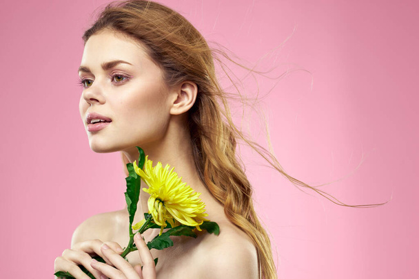 Beautiful girl with a yellow flower on a pink background nude shoulders makeup - Φωτογραφία, εικόνα