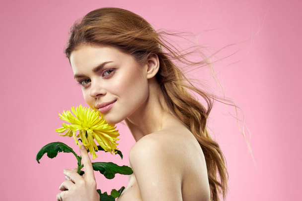 Beautiful girl with a yellow flower on a pink background nude shoulders makeup - Photo, Image