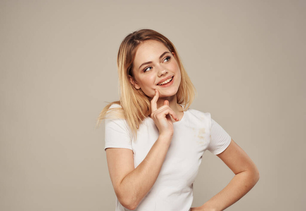 Pretty blonde in a white T-shirt on a beige background touches her face with her hand cropped view - Foto, Imagen