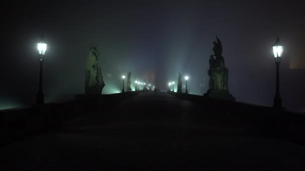 luz vista estática para a lanterna de iluminação pública na Ponte Charles e nevoeiro à noite e silhuetas de pedestres no pavimento de paralelepípedos em Praga. - Filmagem, Vídeo