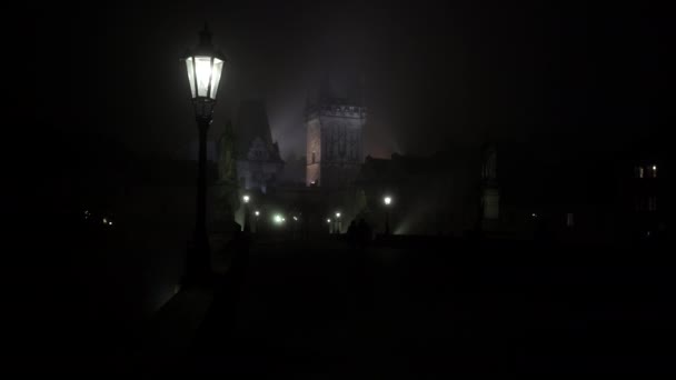 die Laterne der Straßenbeleuchtung auf der Karlsbrücke und der Turm der Kleinseite aus dem 17. Jahrhundert bei Nacht und die Silhouetten der Fußgänger auf dem Kopfsteinpflaster bei Nacht in Prag - Filmmaterial, Video