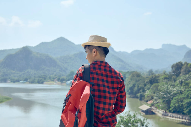 De jonge Aziatische man kijkt uit over de bergen en rivieren - Foto, afbeelding