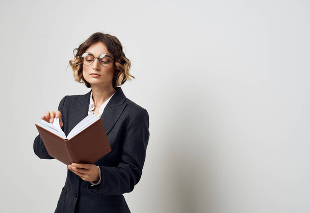Eine Frau im klassischen Anzug mit einem Buch in der Hand und einer Brille auf dem Gesicht - Foto, Bild