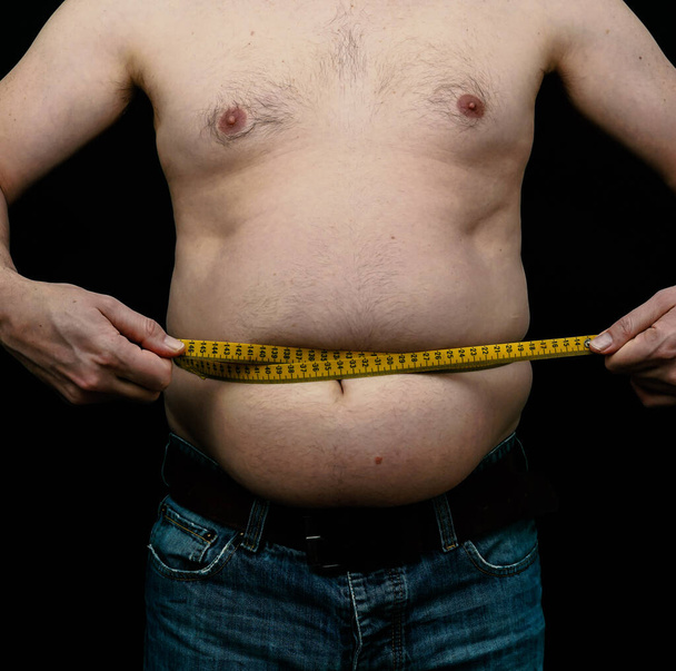太りすぎの男は腹を測定します。黒の背景に隔離されてる。高品質の写真 - 写真・画像