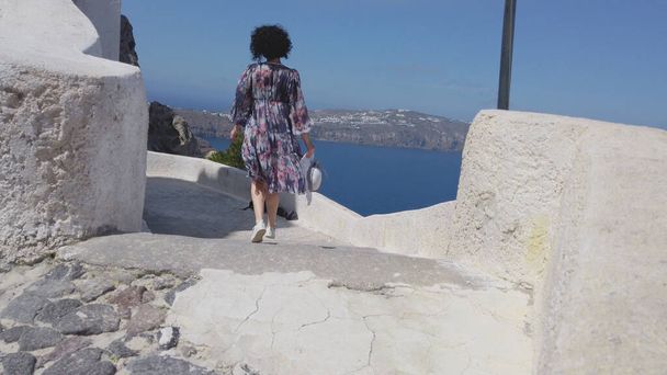 Woman walk at caldera reef edge and look at panoramic Santorini view - Foto, afbeelding