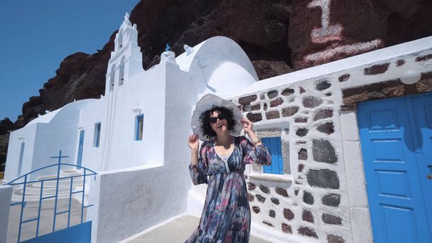 Tourist woman iin dress and hat visiting Saint Nikolaos Orthodox Church located in Akrotiri next to the famous Red Beach at Santorini Island - 写真・画像