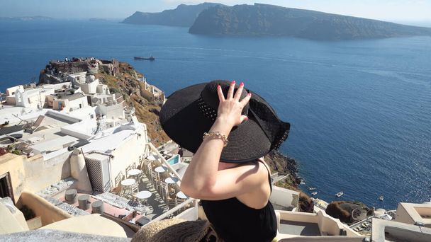 Elegant black dressed woman enjoy view of castle of Oia in Santorini on romantic summer vacation - Photo, image