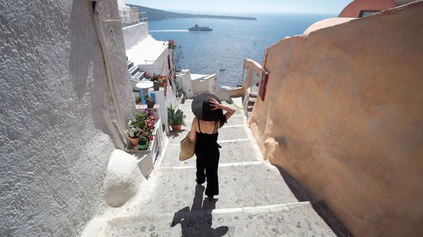 Turista en Oia, Santorini, Grecia. Feliz modelo de moda elegante en negro caminando por las escaleras por famoso destino histórico en Grecia Santorini - Foto, Imagen