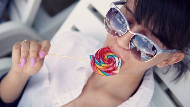 tiener meisje met zonnebril likken lolly en genieten van de zon - Foto, afbeelding