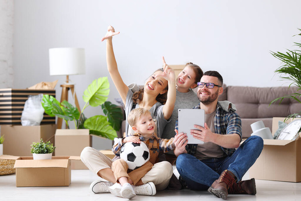 Веселая семья сидит на полу с планшетом и распакованные коробки, обсуждая украшение новой квартиры и указывая - Фото, изображение