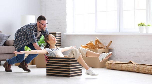 Full body side view of positive young man pushing carton box with laughing woman while having fun together during unpacking things in new home - Фото, изображение