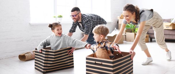 Playful family: parents riding kids in boxes and having fun during moving in new spacious apartment - Fotoğraf, Görsel
