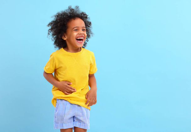 Nadšený malý černý kluk s Afro vlasy v ležérní oblečení se směje a dívá se pryč proti modrému pozadí - Fotografie, Obrázek
