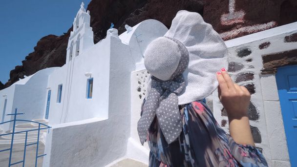 Tourist woman iin dress and hat visiting Saint Nikolaos Orthodox Church located in Akrotiri next to the famous Red Beach at Santorini Island - Foto, imagen