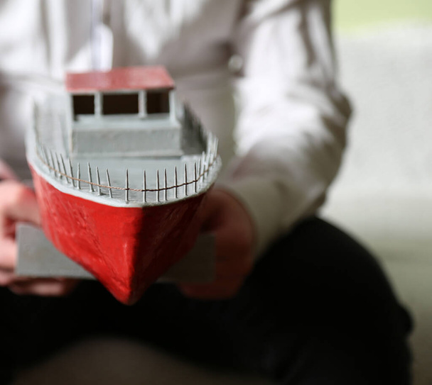 Mladý muž drží v rukou provizorní člun. V rukou toho chlapa je malý motorový člun. Bez tváře. Ručně vyrobeno dítětem. Loď je bílá, červená. Hobby. Vodní doprava. - Fotografie, Obrázek