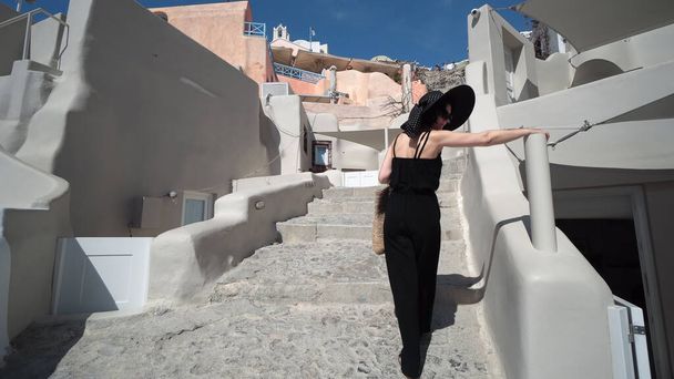 Elegant woman in black climbing stairs on Santorini. Young female is on summer vacation in Santorini. She is visiting famous tourist attraction in Oia - Photo, image