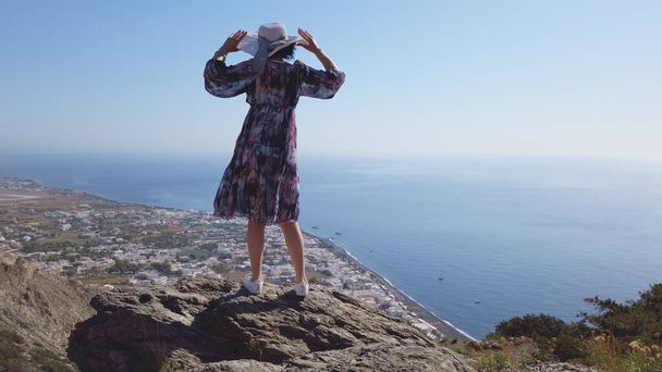 Happy woman tourist having fun swirling around in joy on Santorini. Panoramic view of Kamari from Ancient Thera mountain archeologicl site, slow motion - Foto, afbeelding