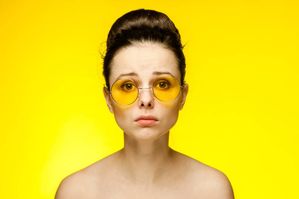 emotional brunette naked shoulders gathered hair in a bun yellow background - Фото, зображення