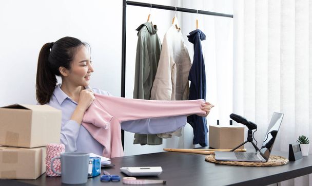 Young Asian women show off the clothes customers want to see through a live performance with a laptop, Selling things through video recording or live shows via the Internet, Top business. - 写真・画像