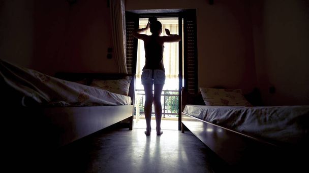Sylwetka kobieta otwierając zasłonę w sypialni i wyciągając po wstaniu rano - Zdjęcie, obraz