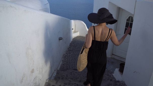 Elegant woman black dressed walk on narrow street stairs in Santorini, Greecce. Tourist visitin Santorini landmarks in Oia - Photo, Image