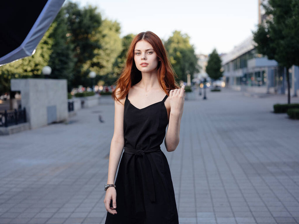 beautiful woman in a black dress walks in the park and green trees in the background - Фото, изображение