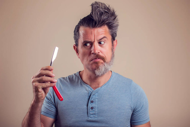 Ein Porträt eines Mannes mit Halbbart und Haaren hält Rasiermesser in der Hand - Foto, Bild