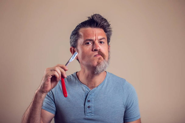 Un retrato de hombre con media barba y pelo sostiene una navaja en su mano - Foto, Imagen