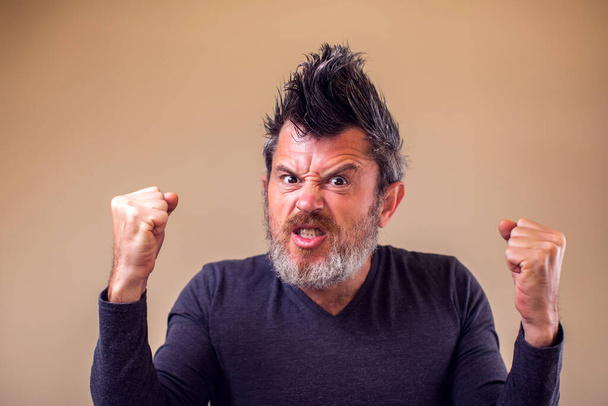 Closeup portrait of an angry adult man with a beard and iroquois shows fist. People and emotions concept - Photo, image