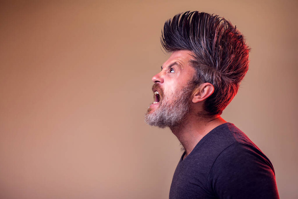 Portrait rapproché d'un homme adulte en colère avec une barbe et des iroquois. Concept des personnes et des émotions - Photo, image