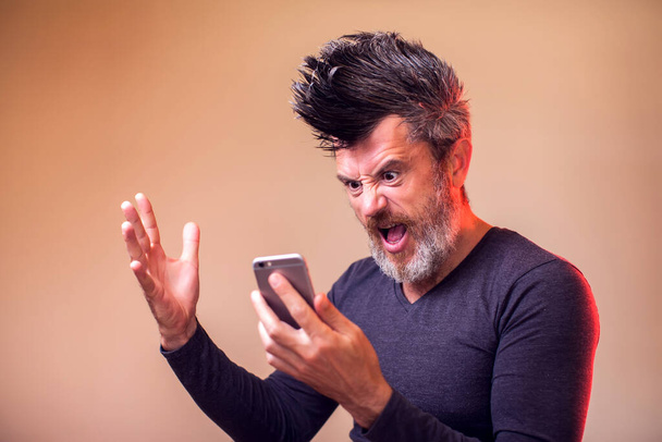 Un uomo arrabbiato con barba e irochese che urla al telefono. Persone, emozioni concetto - Foto, immagini