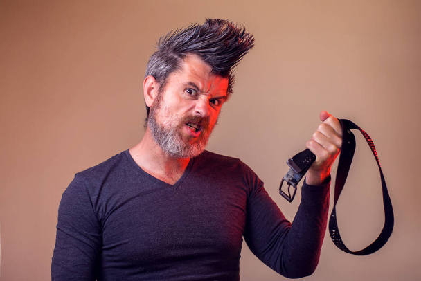 Angry bearded man holds belt in hand. Emotions and family violence concept - Photo, Image