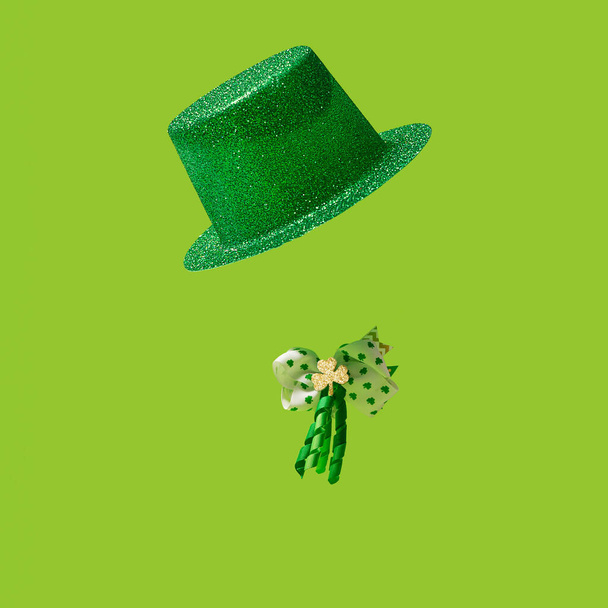 Patrick 's Day concept. Ierse glitterhoed, en strik met klaverblad klavertjes in goud en groene kleuren, en krullint In op groene achtergrond. - Foto, afbeelding