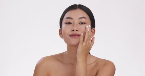 Cuidado de belleza. Retrato de mujer asiática joven aplicando crema de cuidado en la cara, fondo de estudio blanco, cámara lenta - Metraje, vídeo