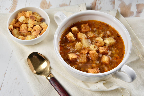 Sopa de cereales y legumbres servida en un tazón con pan crutones cerca - Foto, Imagen