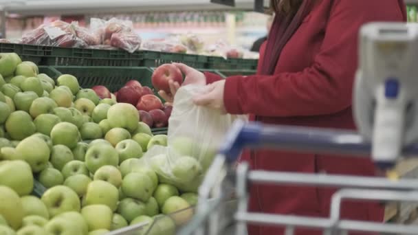 Una ragazza al supermercato compra mele. Ha messo della frutta nella borsa. In primo piano c'è il carrello - Filmati, video