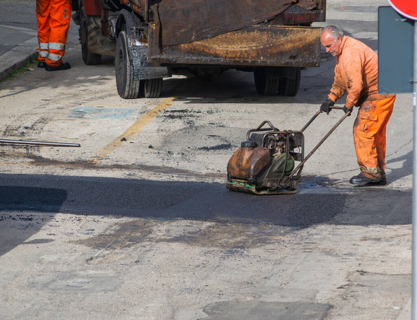 Trabajador regular la colocación de asfalto nuevo para parchear un bache en la carretera. - Foto, imagen