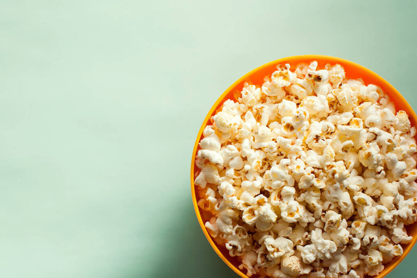 An orange bowl with popcorn isolated on green background. Food concept - 写真・画像
