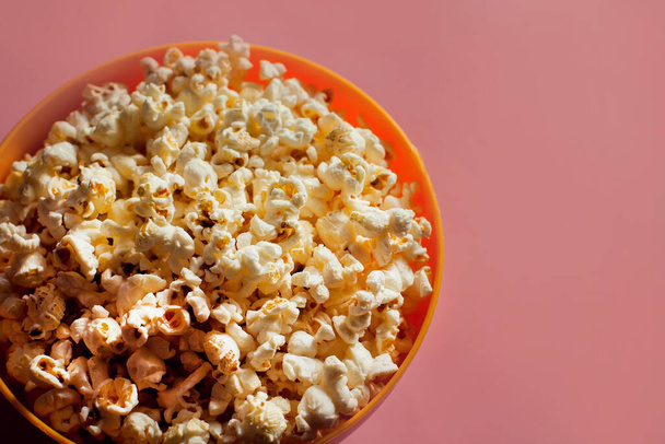 Egy narancssárga tál popcornnal, rózsaszín háttérrel. Élelmiszer-koncepció - Fotó, kép
