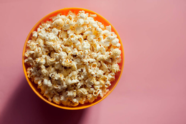 An orange bowl with popcorn isolated on pink background. Food concept - 写真・画像