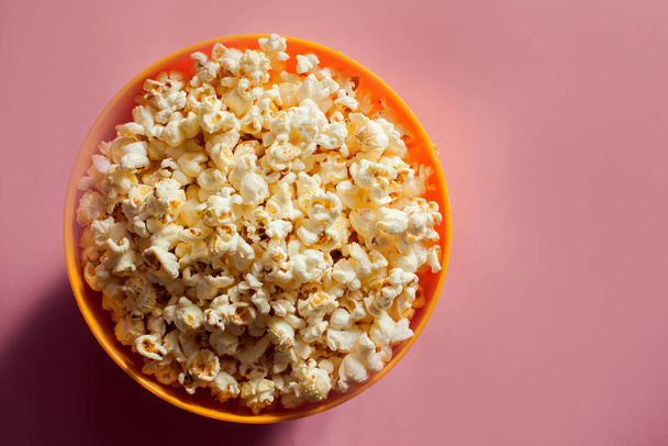 Oranžová mísa s popcornem izolovaným na růžovém pozadí. Koncept potravin - Fotografie, Obrázek