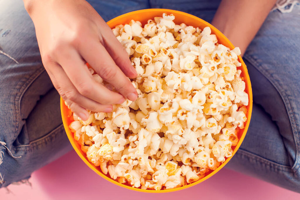 Woman in jeans holding bowl with popcorn over pink background. Food and enternaiment concept - Photo, Image