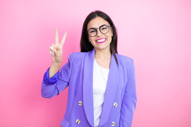 Young business woman wearing purple jacket over pink background showing and pointing up with fingers number two while smiling confident and happy - Photo, Image