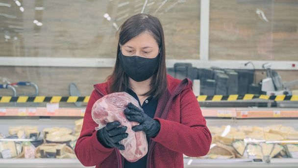 Женщина в маске и перчатках против вируса выбирает свинину в продуктовом магазине - Фото, изображение
