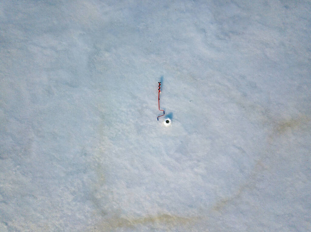 Tornillo de hielo manual en el hielo cerca del agujero. Vista aérea del dron. Mañana soleada de invierno. - Foto, Imagen