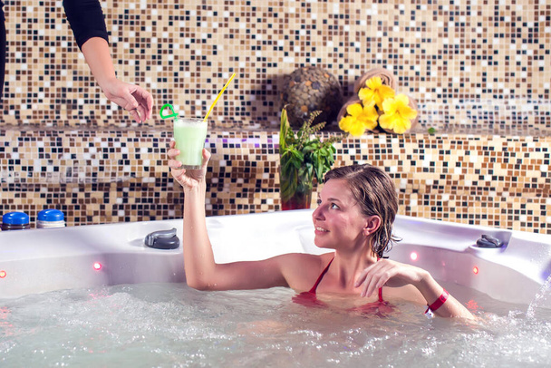 Beautiful spa. Young woman in red bikini enjoying Jacuzzi and drink fresh juice in a spa center - Photo, Image