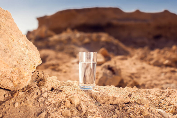Glass with water on sand in the desert. Thitsty, heat and drought concept - Photo, Image